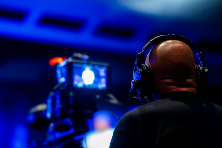 A videographer wearing headphones captures an event with professional video equipment in a dimly lit setting.