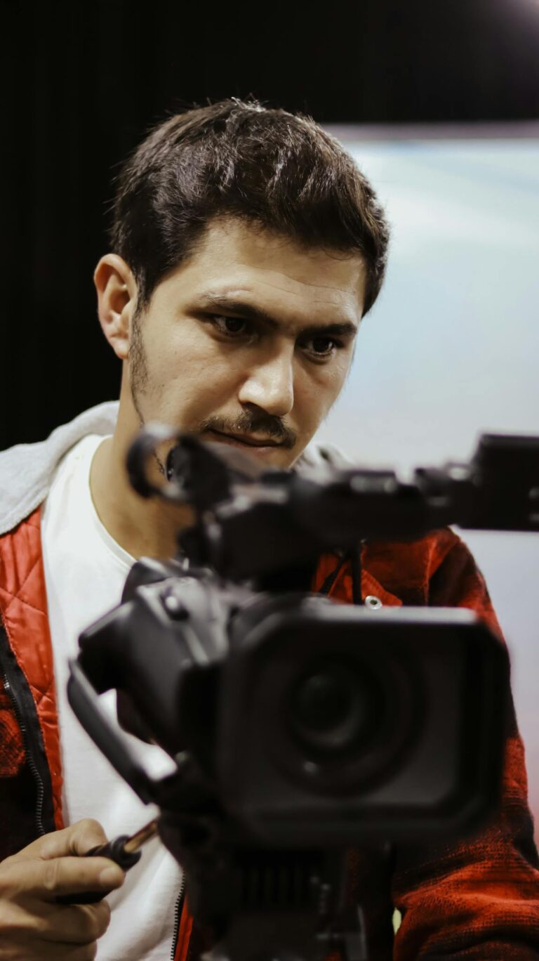 Cameraman with short black hair operates a professional video camera indoors.